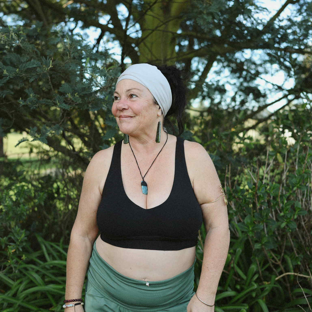Woman in black sports bra and green pants standing outdoors with trees in the background