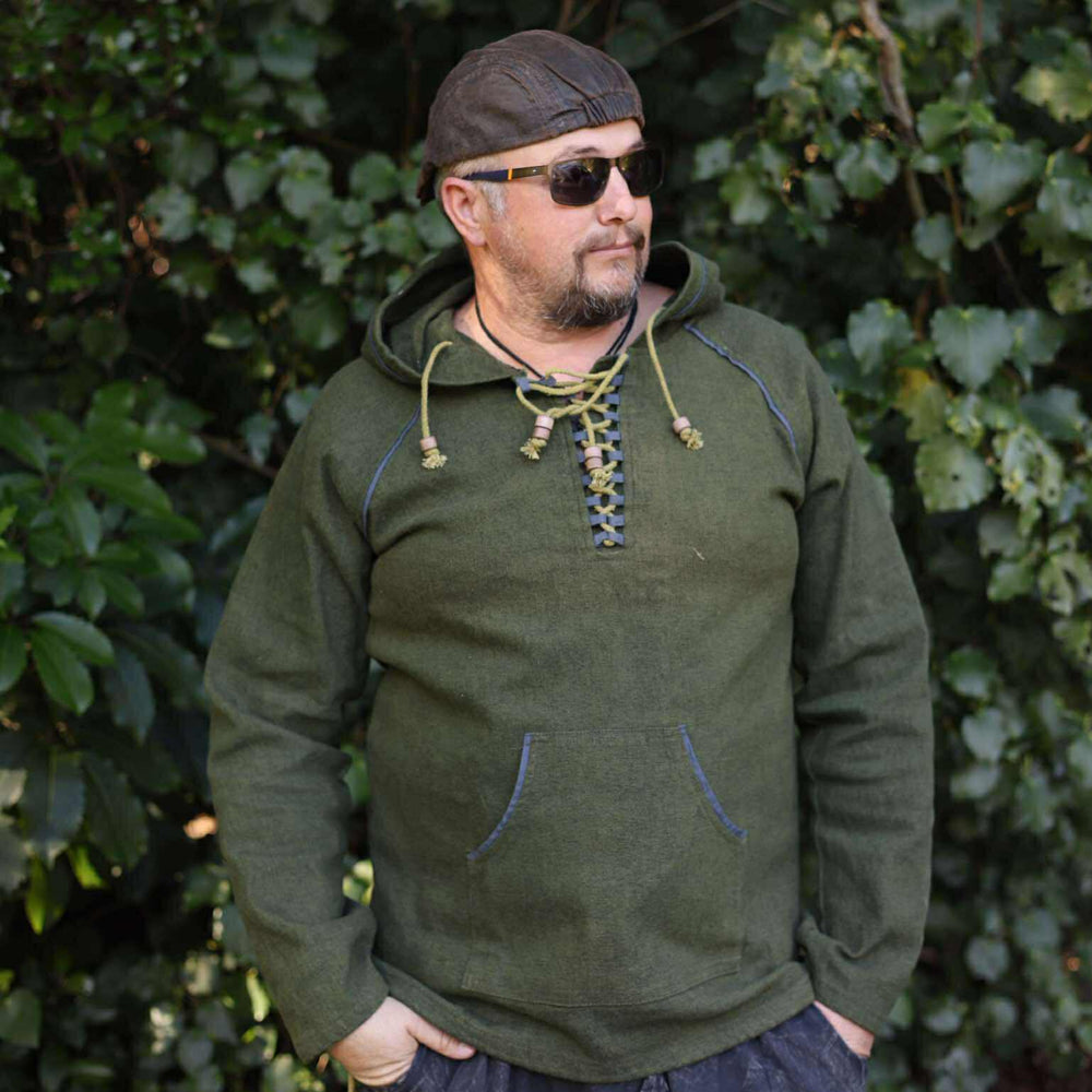 Man wearing a green hooded sweatshirt and sunglasses standing in front of green foliage.