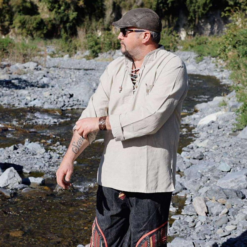 
                  
                    Load image into Gallery viewer, Man standing by a river wearing a beige jacket and dark pants with patterns, surrounded by greenery.
                  
                