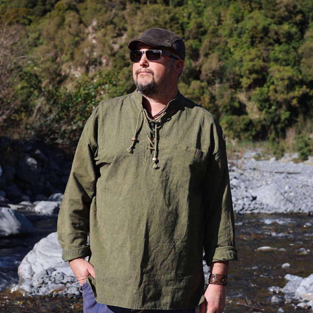 
                  
                    Load image into Gallery viewer, Man in a green shirt standing by a river with trees in the background
                  
                
